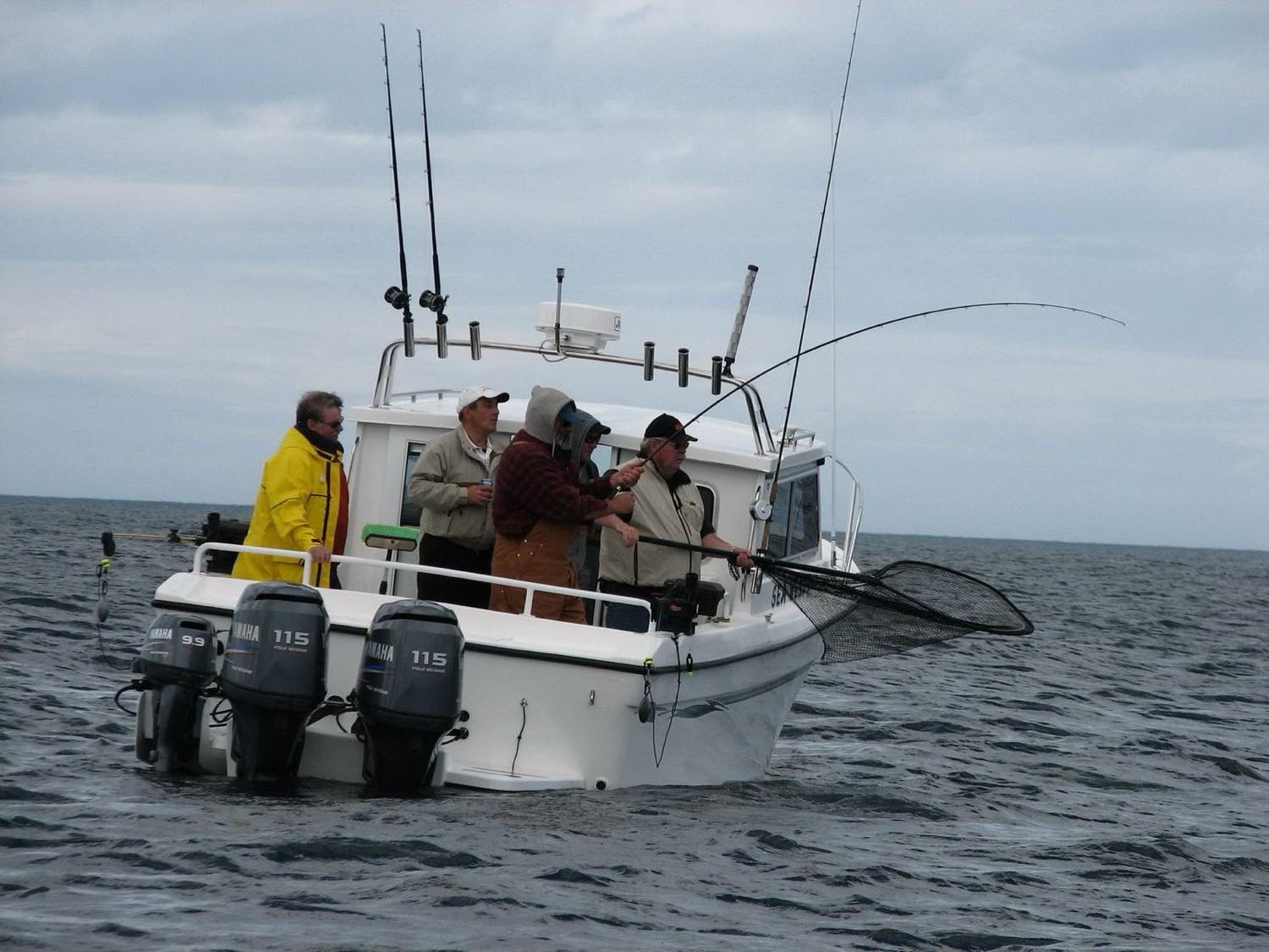 Guests netting a fish at the side of a white hard-top charter boat