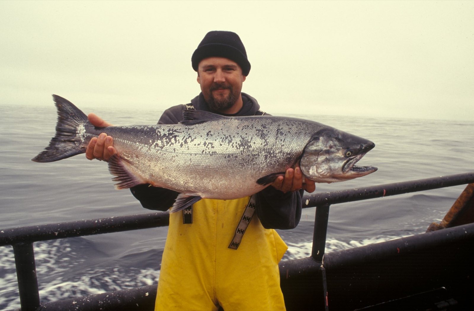 Angler in yellow bibs holding a large Chinook salmon at sea